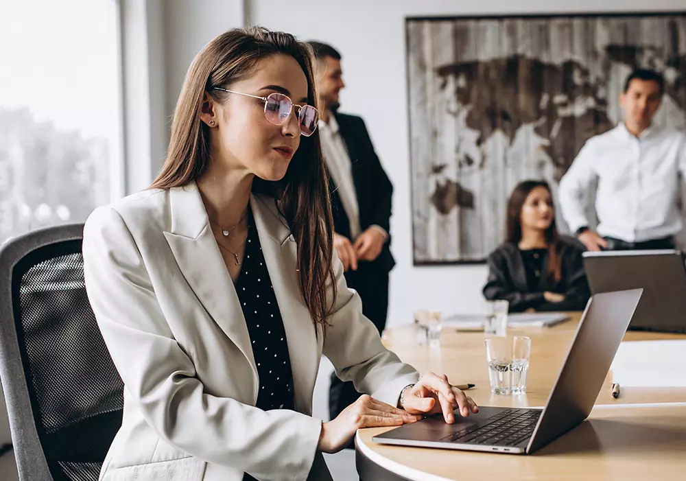 Empresarios en una junta directiva. Mujer en primer plano revisando su computadora Empresarios en una junta directiva. Mujer en primer plano revisando su computadora