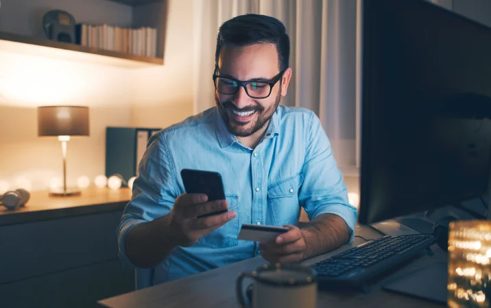 Hombre realizando compras en la computadora de noche con su tarjeta