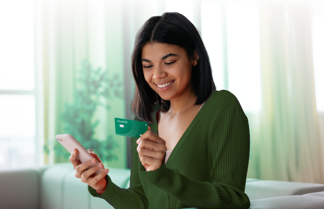 Mujer alegre con su tarjeta de débito LAFISE enviando remesas con su celular por medio de la banca en línea de Banco LAFISE