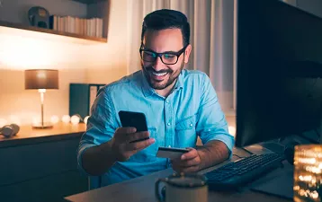 Hombre realizando compras en la computadora de noche con su tarjeta
