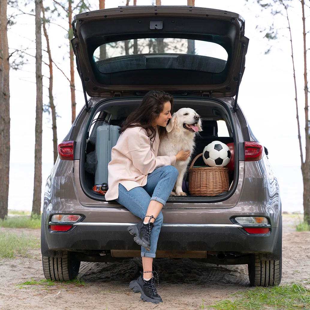 Mujer sentada en maletero de camioneta con su perro en un día de campo.