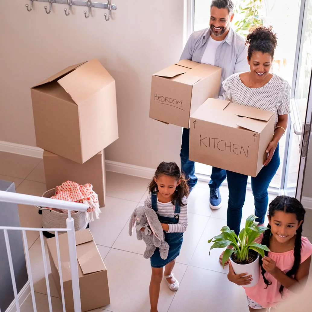 Familia feliz entrando a casa con cajas de mudanzas.