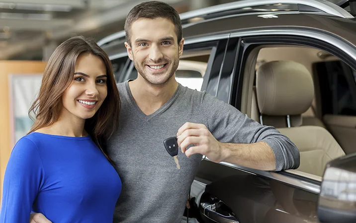 Pareja sonriendo a lado de su nuevo auto.