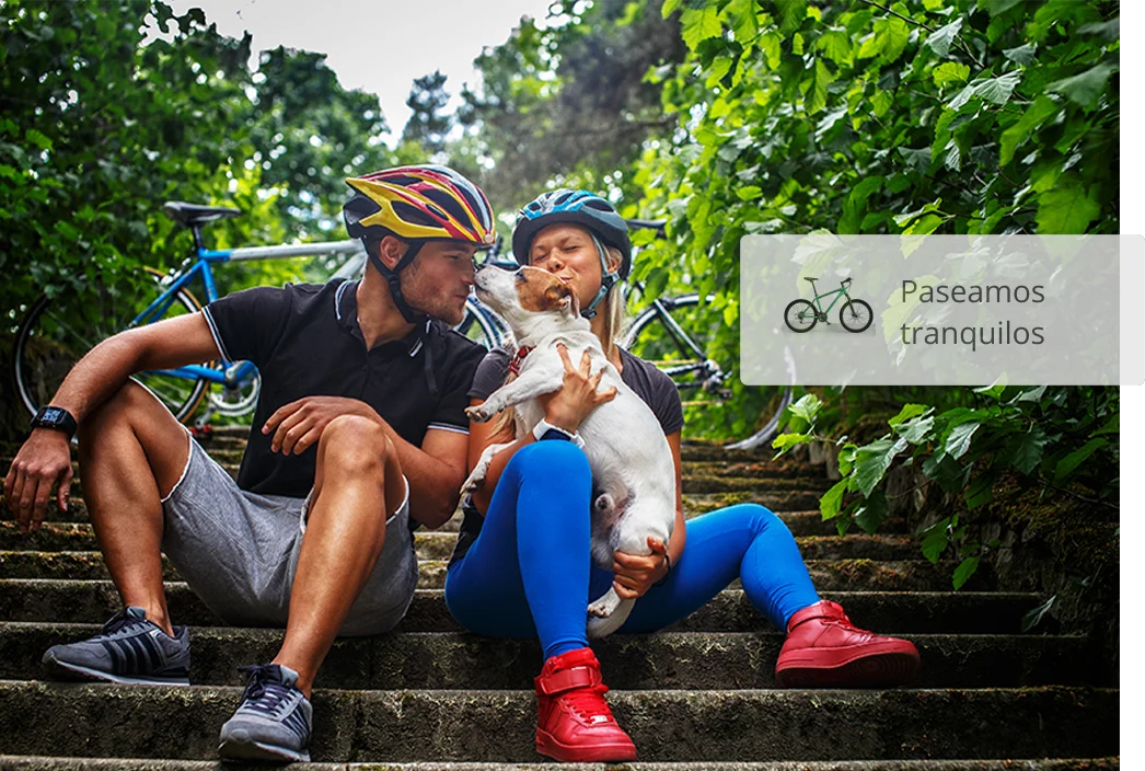 Pareja de ciclistas sentados delante de sus bicicletas, acariciando un perro