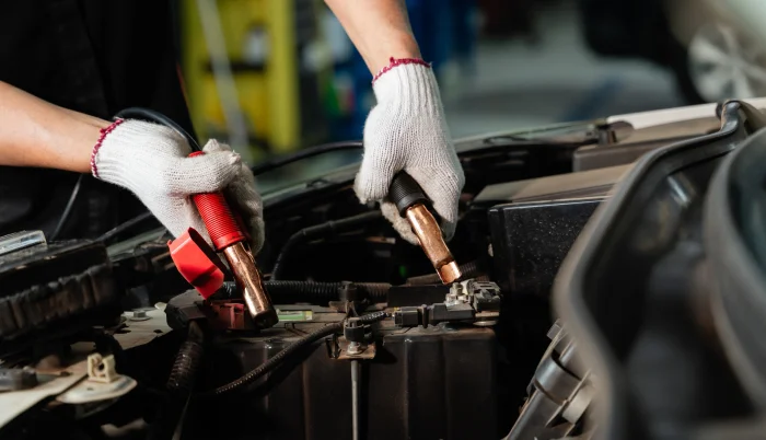 Manos de mecánico pasando corriente a batería de auto.