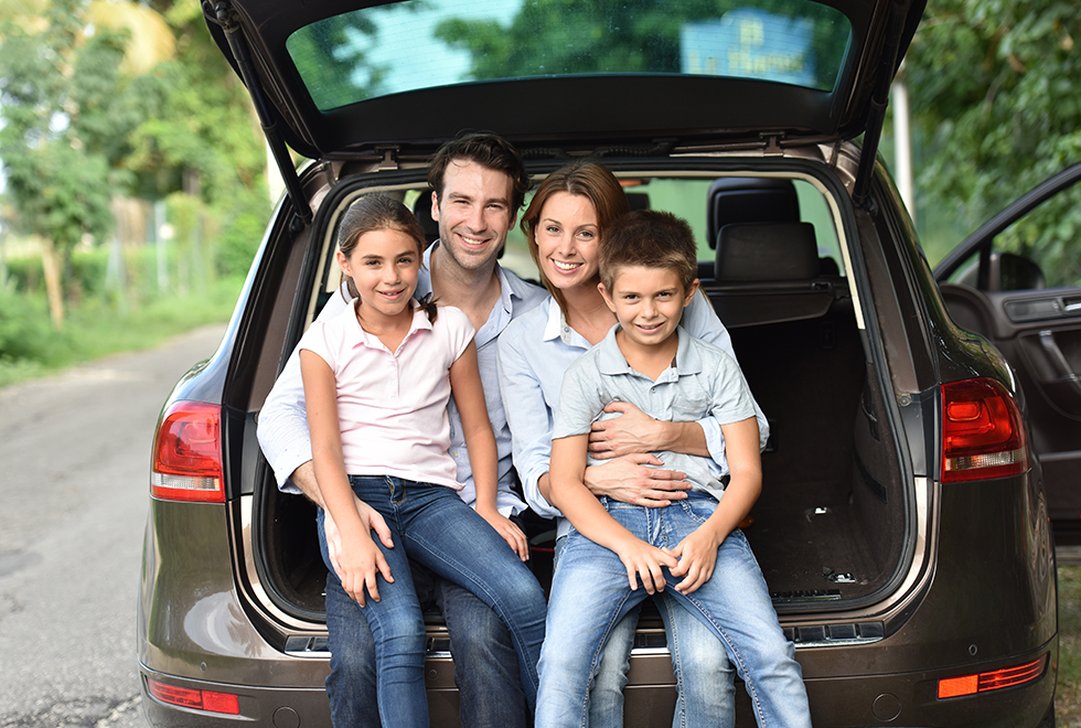 Familia sonriente sentada en el maletero de auto